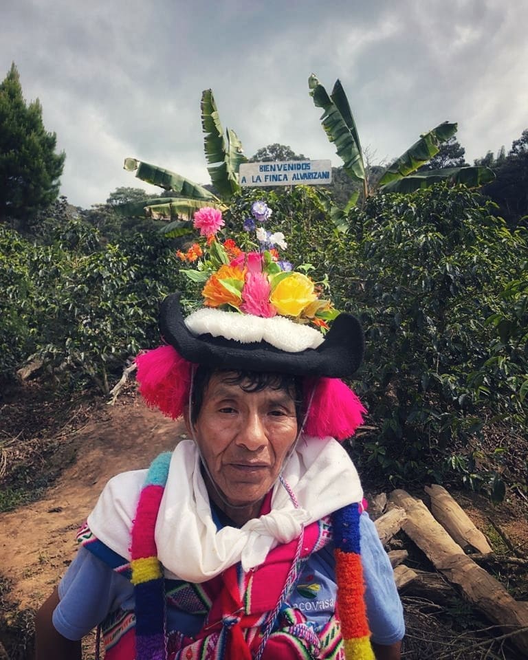 Person wearing a colorful traditional hat with flowers in a coffee plantation setting
