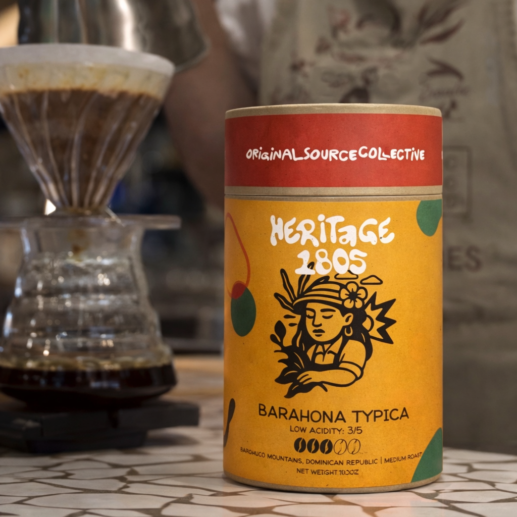 Coffee canister with 'Heritage 1805' branding on a table with a blurred coffee-making setup in the background.